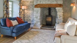 A living room with a stone fireplace, blue and white sofas, a patterned rug, and a floor lamp. - 2 bedroom accommodation in Bodmin (Bodmin)