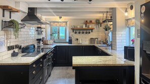 A modern kitchen with black cabinets, granite countertops, a built-in oven, and a window overlooking a garden. - 2 bedroom accommodation in Bodmin (Bodmin)