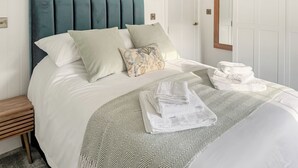 A neatly made bed with a green upholstered headboard, a patterned throw blanket, and folded towels on the side. - 2 bedroom accommodation in Bodmin (Bodmin)