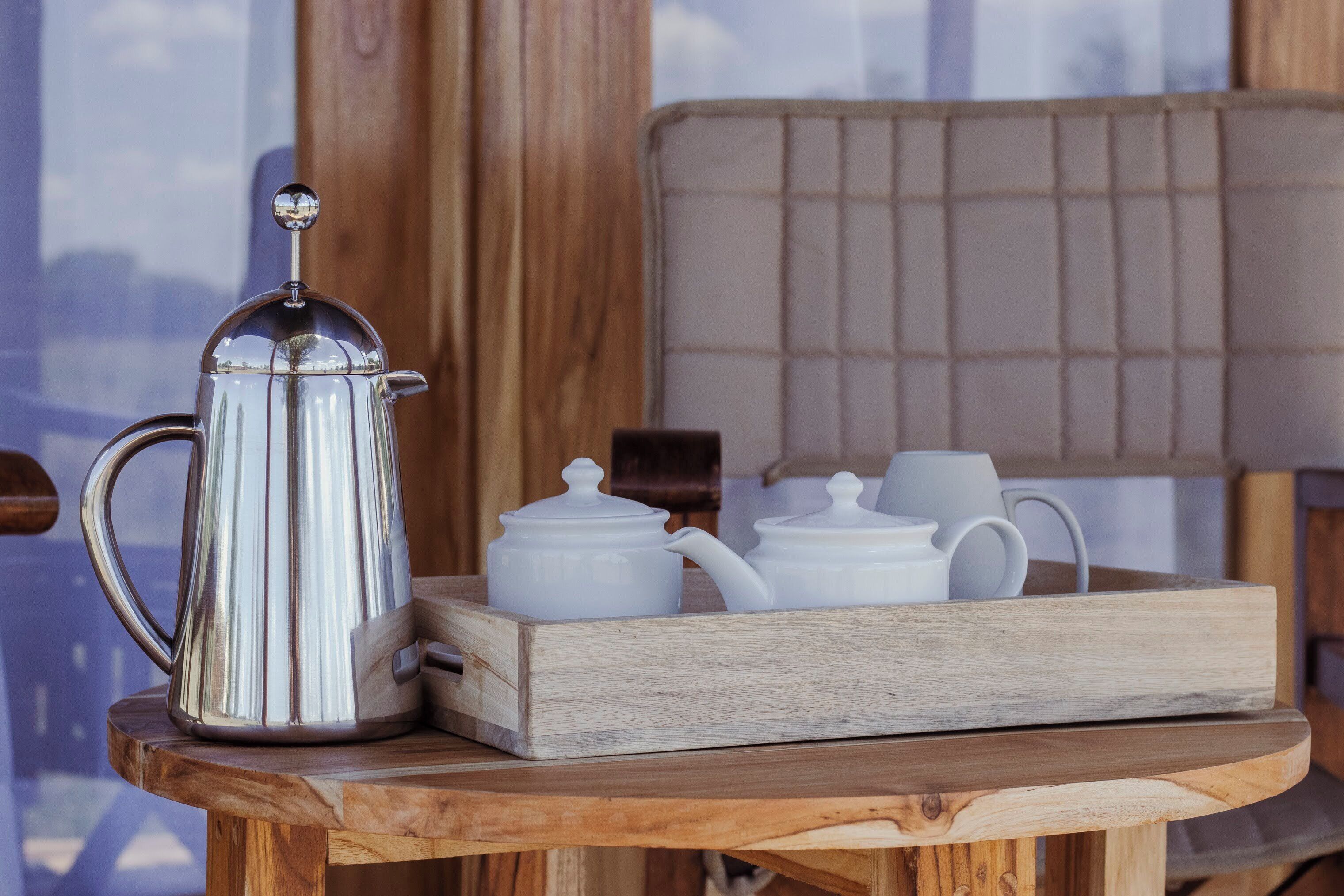 A wooden table with a metal coffee pot, white teapots, and cups.