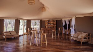 A spacious room with wooden furniture, a bar area, and large windows. - Conserve Safari Serengeti (Serengeti)