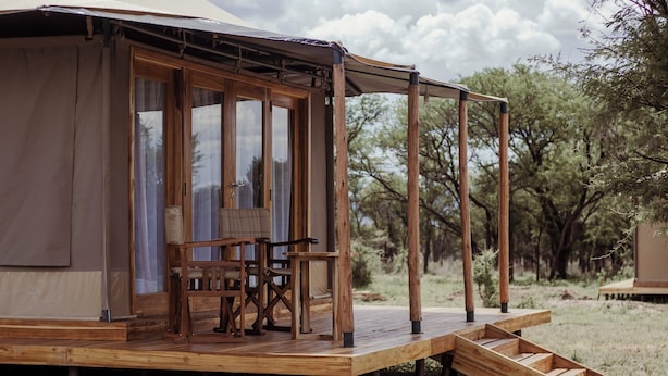 A wooden deck with outdoor furniture, a staircase leading to a covered area, and a natural landscape in the background. - Conserve Safari Serengeti (Serengeti)