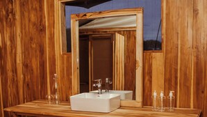 A wooden bathroom with a large mirror, a sink, and a towel rack. - Conserve Safari Serengeti (Serengeti)