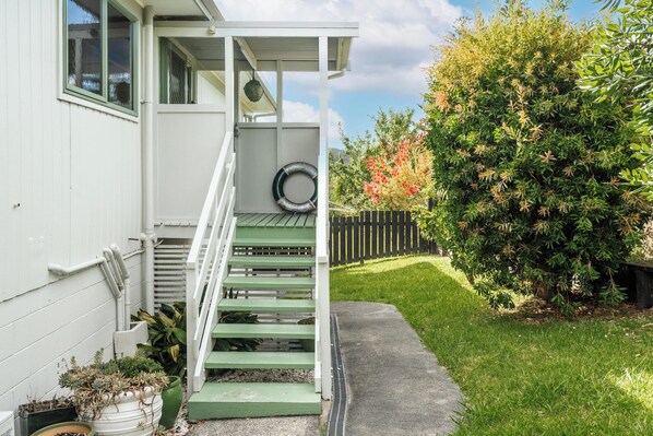A white house with a green staircase leading to a porch, surrounded by a well-maintained garden and a wooden fence. - Russell HQ (Russell)