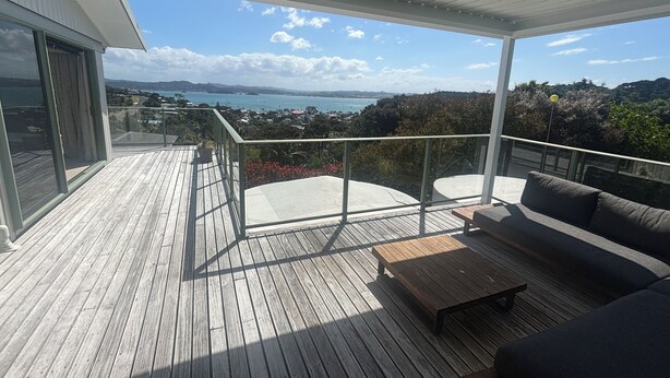 Eine Holzterrasse mit Glastrennwand, einer Couch und einem Tisch.