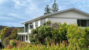 Ein modernes, zweistöckiges Haus mit Balkon, umgeben von üppiger Vegetation und Bäumen.