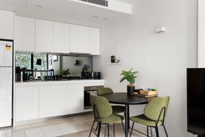 Een moderne keuken met witte kasten, een zwart aanrecht en een eethoek met twee groene stoelen.