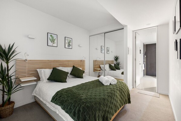 A modern bedroom with a wooden headboard, a green blanket, and a mirror.