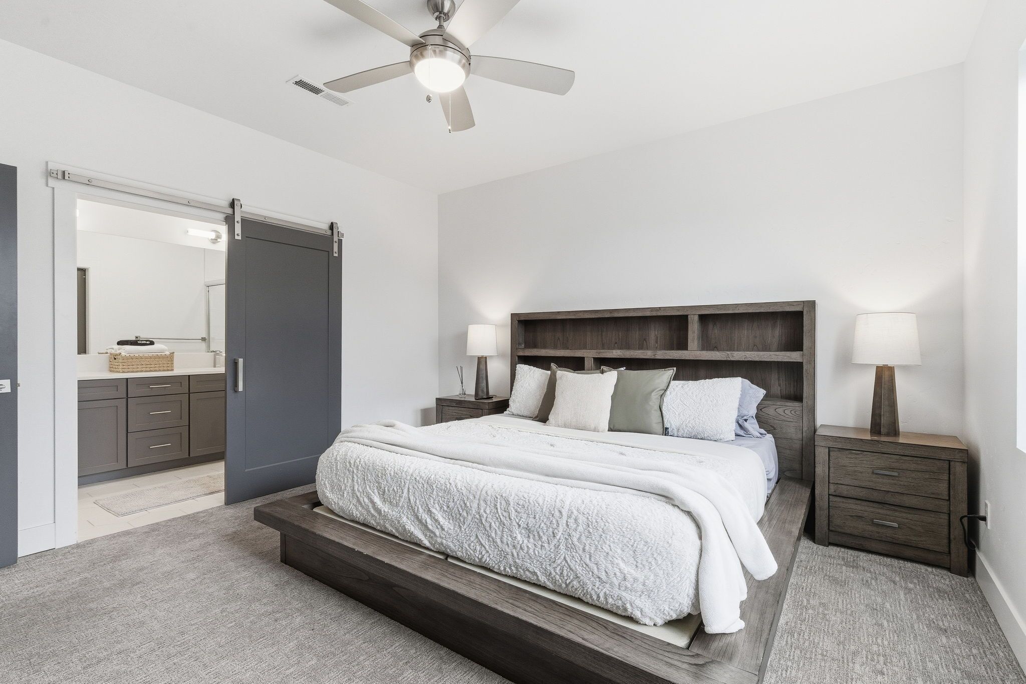 Une chambre à coucher comprenant un lit, des tables de chevet, un ventilateur de plafond et une armoire.