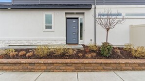 A modern two-story house with a grey door, a small window, and a tree in the front yard. - Modern Meridian Retreat - Spacious 4 Bedroom - Walkable Downtown (Meridian)