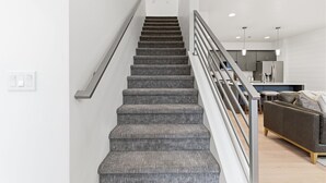 A staircase with a metal railing leading to a modern kitchen area. - Modern Meridian Retreat - Spacious 4 Bedroom - Walkable Downtown (Meridian)