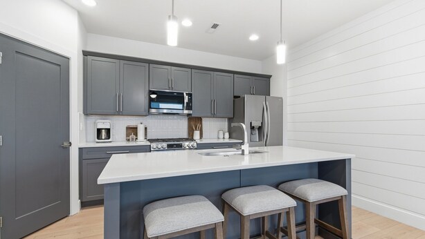 A modern kitchen with grey cabinets, a white island, and two bar stools. - Modern Meridian Retreat - Spacious 4 Bedroom - Walkable Downtown (Meridian)