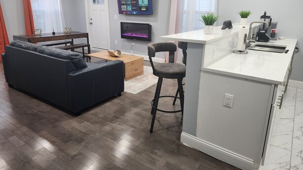 Een moderne woonkamer met een zwarte leren bank, een houten salontafel en een aan de muur bevestigde televisie.