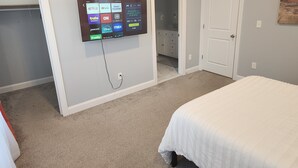 Een slaapkamer met een bed, een aan de muur bevestigde televisie waarop diverse streamingdiensten te zien zijn, en een deur naar een badkamer.