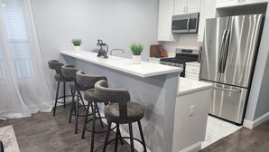Een moderne keuken met een centraal eiland, een bar met krukken, roestvrijstalen apparatuur en een wit aanrecht.