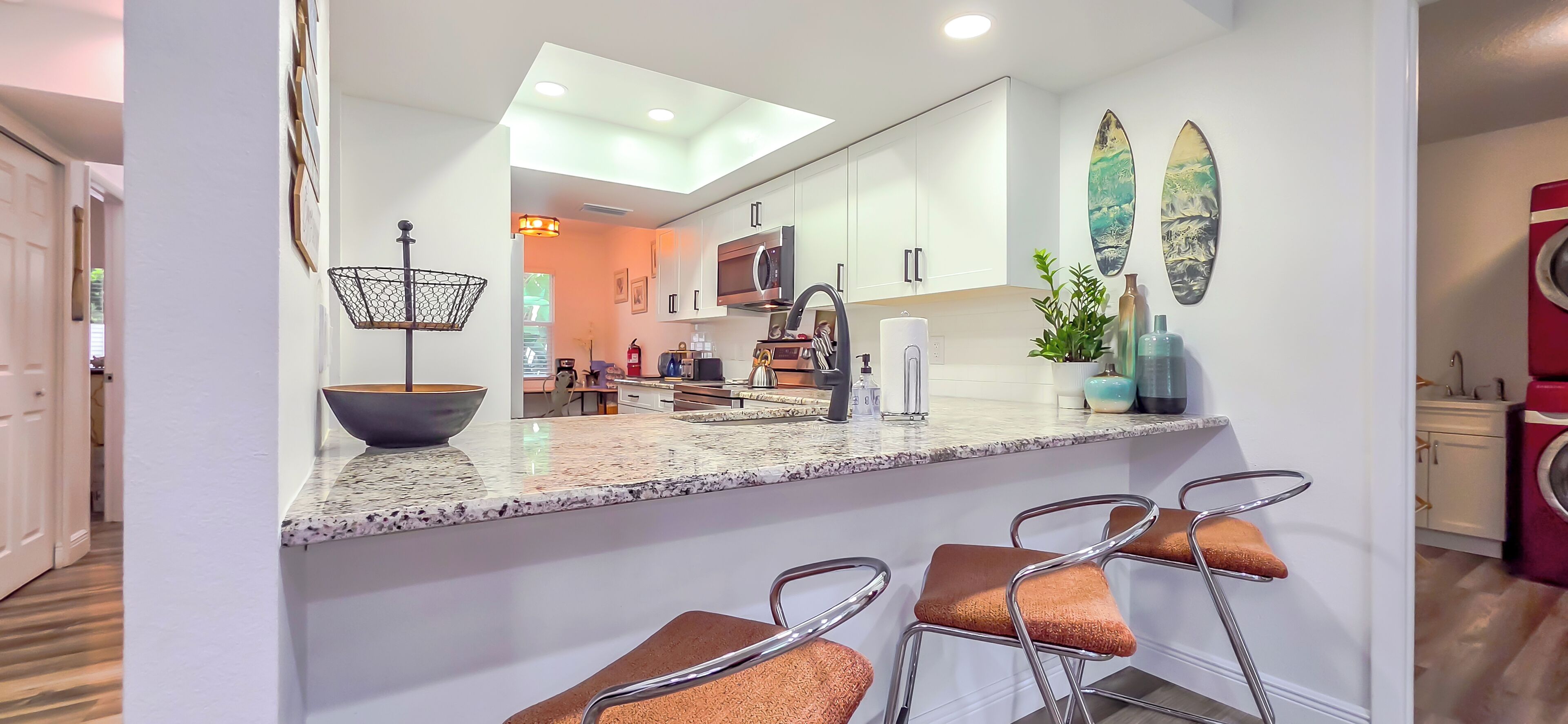 A modern kitchen with a granite countertop, stainless steel appliances, and a bar area with stools.