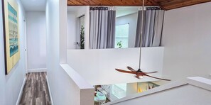 Un intérieur moderne avec un ventilateur de plafond, un coin repas comprenant une table et des chaises, et une vue sur l’extérieur par une fenêtre agrémentée de rideaux.