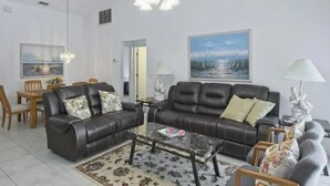 A living room with a sofa, coffee table, and a dining area with chairs and a table.