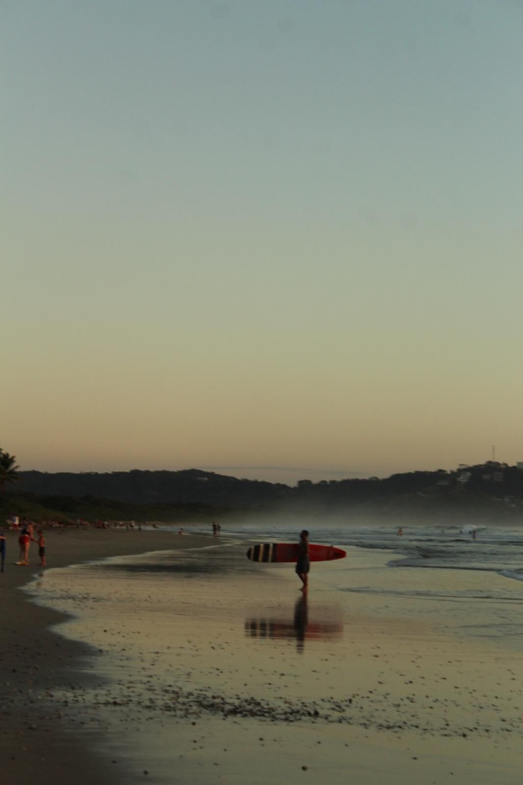 Escena de playa con una persona llevando una tabla de surf.