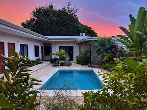 A modern house with a swimming pool, surrounded by tropical plants and a sunset sky. - Hotel Huacas (Tamarindo)
