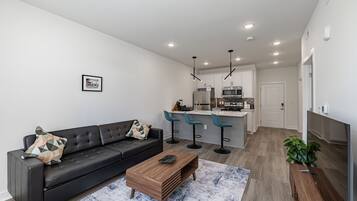 Una sala de estar moderna con un sofá de cuero negro, una mesa de centro de madera y un tapete azul estampado.