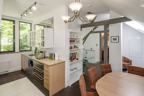 Een moderne keuken met witte kasten, een houten aanrecht en een eethoek met een ronde tafel en bruine stoelen.
