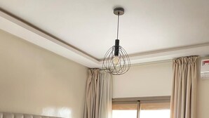 Un dormitorio con cabecera capitonada, cama grande con ropa de cama estampada, lámpara colgante y vistas a un balcón con planta en maceta.