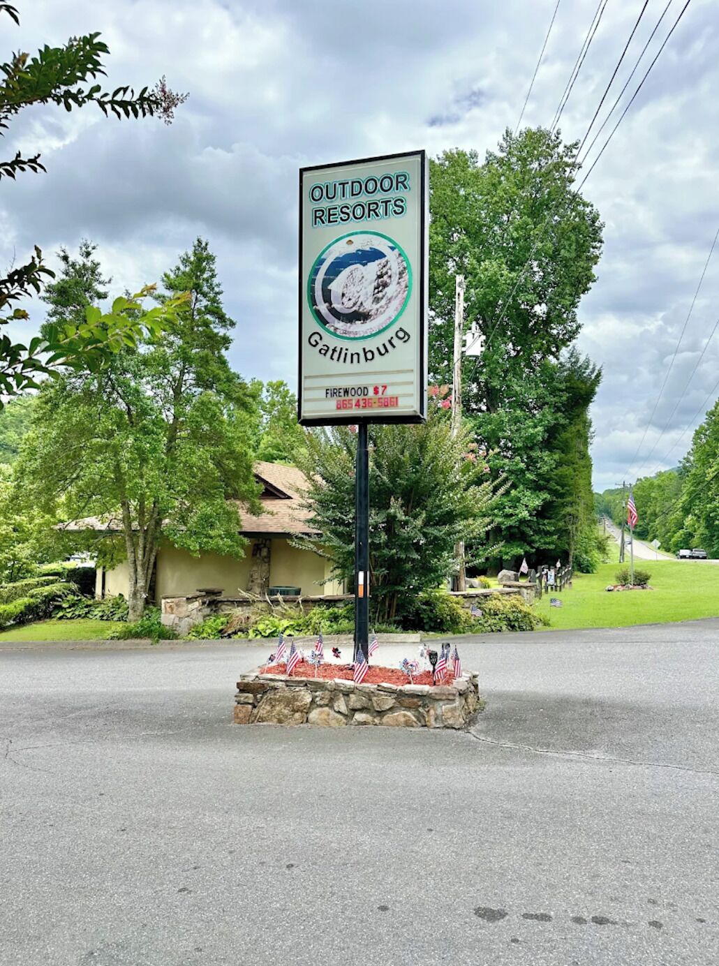 En skylt för semesteranläggningar utomhus i Gatlinburg, med en bas av sten och amerikanska flaggor.