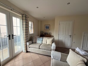 A living room with a sofa, a smaller couch, a door, and a window with curtains. - Comfortable retreat with sea views in friendly Scottish village (Garlieston)