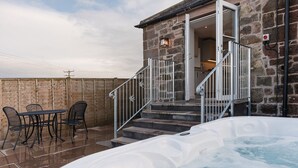 A stone building with a hot tub and outdoor seating. - Cosy Northumberland farm cottage with hot tub in quiet location (Berwick-upon-Tweed)