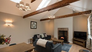Ein Wohnzimmer mit freiliegenden Holzbalken, einem Kamin, einer Couch, einem Fernseher und einem Essbereich.
