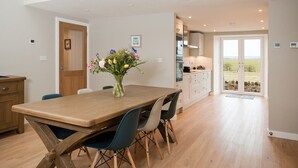 Eine moderne Küche mit Holztisch und -stühlen, einem Blumenstrauß und Blick ins Freie durch eine Glastür.