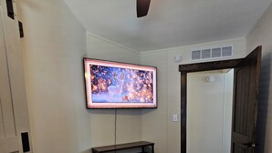 Una camera d'albergo con un letto, una televisione a muro, una panca in legno e una porta.