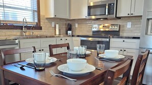 Una cucina moderna con mobili bianchi, un tavolo da pranzo in legno apparecchiato con piatti, ciotole e bicchieri, e un forno a microonde in acciaio inossidabile sopra il piano di lavoro.