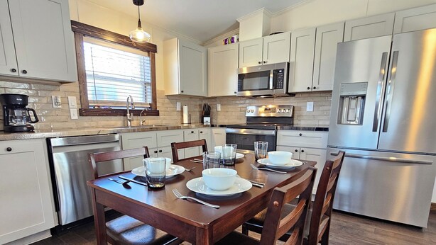Una cucina moderna con mobili bianchi, elettrodomestici in acciaio inossidabile e un tavolo da pranzo in legno apparecchiato per quattro persone.