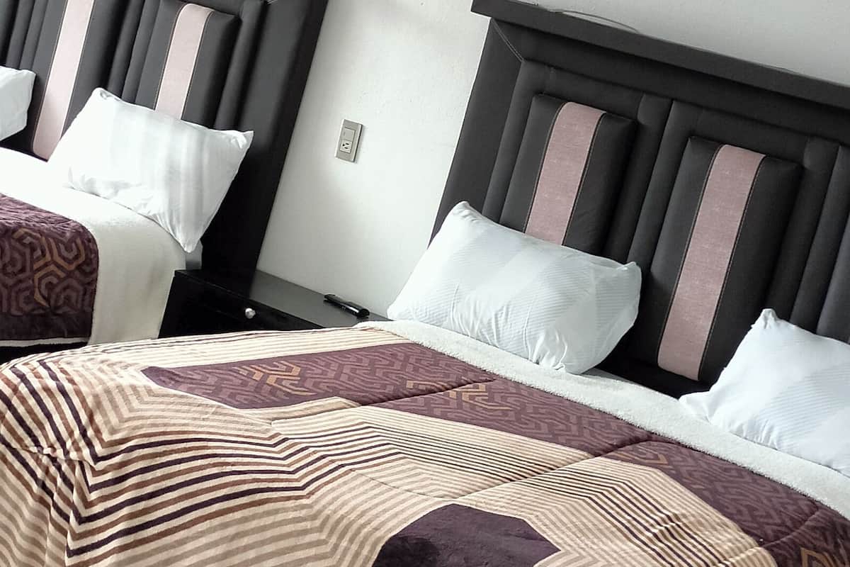 Hotellihuone, jossa on kaksi sänkyä. Jokaisessa sängyssä on pääty, suuri peitto ja yöpöytä, jossa on lamppu.