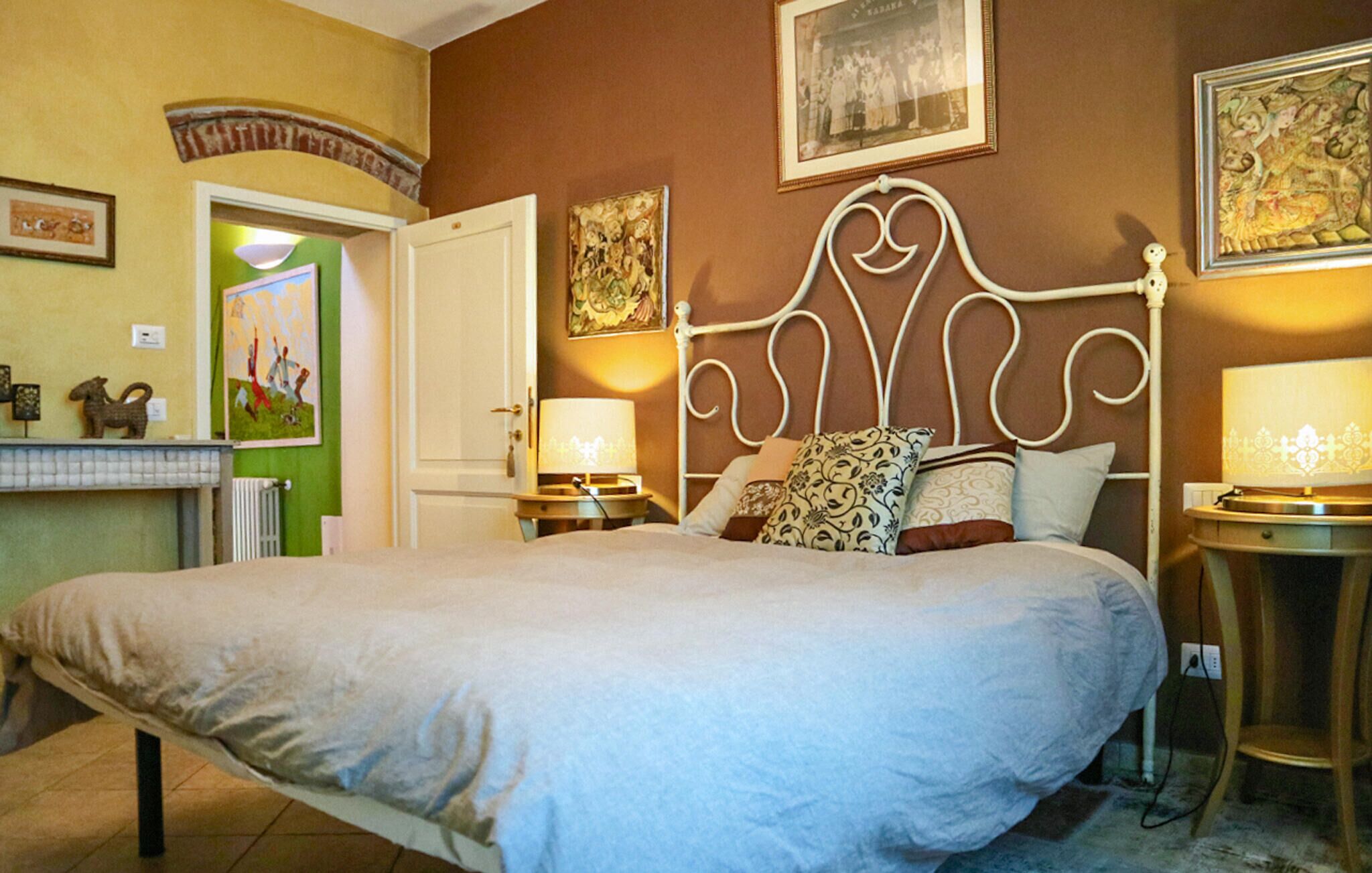 Een slaapkamer met een groot bed, twee nachtkastjes met lampen, een deur en een muur met ingelijste foto's.