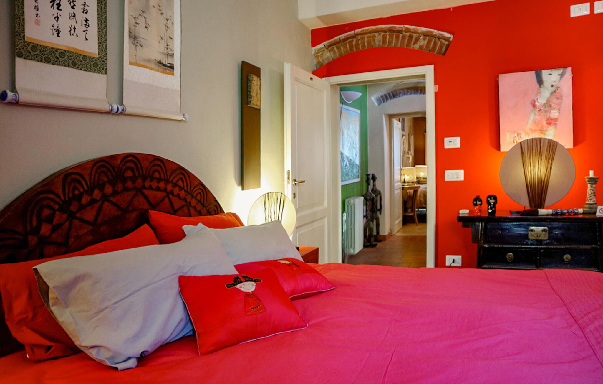 Een slaapkamer met een rode sprei, een houten hoofdbord en een spiegel op een dressoir.