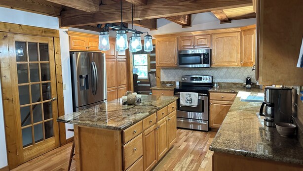 A modern kitchen with wooden cabinets, stainless steel appliances, granite countertops, and a large island. - Big Kahuna Mauka, Beautiful Mountain View 4-BR Cabin in charming Waynesville (Waynesville)