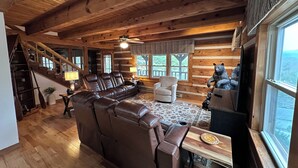 A cozy log cabin interior with a leather sofa, a wooden dining table, and a bear sculpture. - Big Kahuna Mauka, Beautiful Mountain View 4-BR Cabin in charming Waynesville (Waynesville)