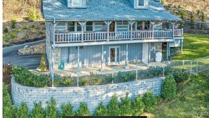 A two-story house with a balcony, a stone retaining wall, and a fenced yard. - Big Kahuna Mauka, Beautiful Mountain View 4-BR Cabin in charming Waynesville (Waynesville)