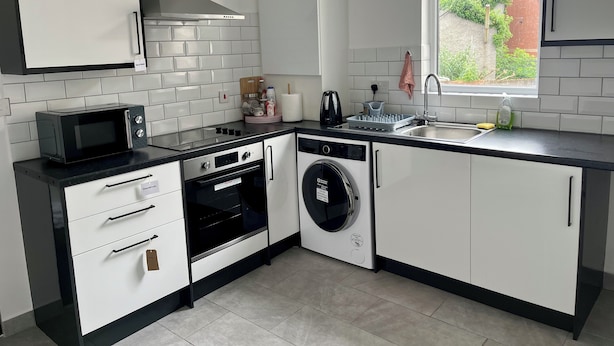 A modern kitchen with white cabinets, a black countertop, a microwave, a dishwasher, and a window with a view of greenery outside.