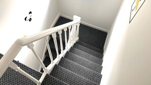 A staircase with a white railing, carpeted steps, and a wall with a window and a poster.