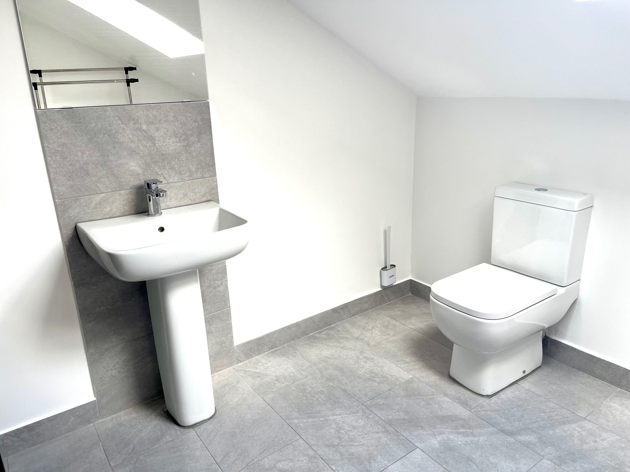 Un baño moderno con lavamanos pedestal, inodoro y perchero para toallas.