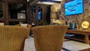 A cozy room with a large woven chair, a smaller woven stool, and a decorative wall-mounted shelf with a television displaying a scenic view. - Refugio Do Frances Ghesthouse (São Sebastião)