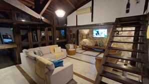 A cozy living room with a sofa, a television, a stone fireplace, and a wooden staircase. - Refugio Do Frances Ghesthouse (São Sebastião)