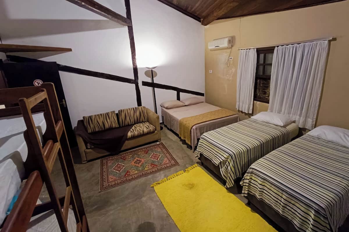 A room with a sofa, two single beds, a small table, and a ceiling fan.