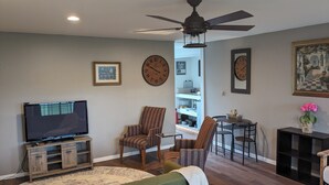 Una sala de estar con televisor, ventilador de techo y comedor con sillas y mesa.
