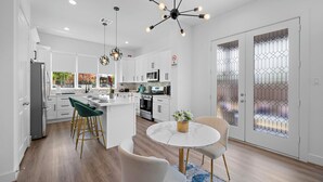 Een moderne keuken met witte kasten, een centraal eiland en een eethoek met een ronde tafel en stoelen.
