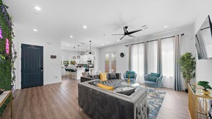 Een moderne woonkamer met een grijze modulaire bank, een klein bijzettafeltje en een blauwe fauteuil. In de achtergrond bevindt zich een keuken met witte kasten en een eethoek.